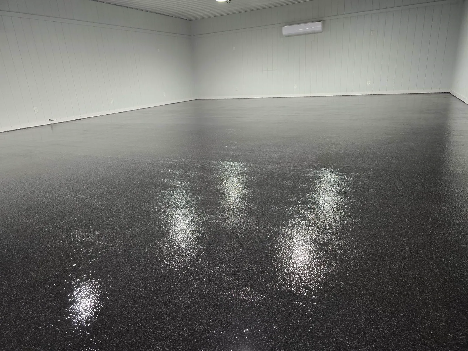 A large empty shop with a dark flake epoxy floor, freshly finished and reflecting the overhead lights.
