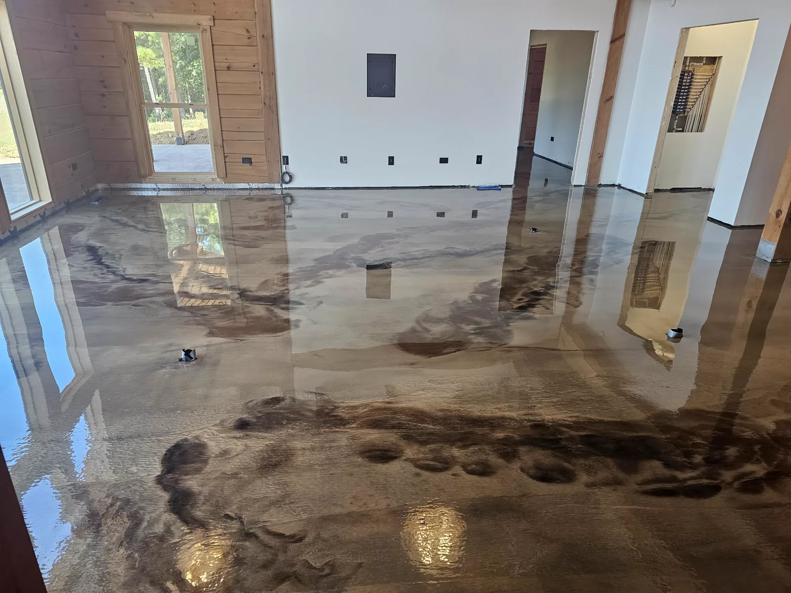 A large open room with a brown and cream metallic epoxy floor, doorways and windows reflected in it.