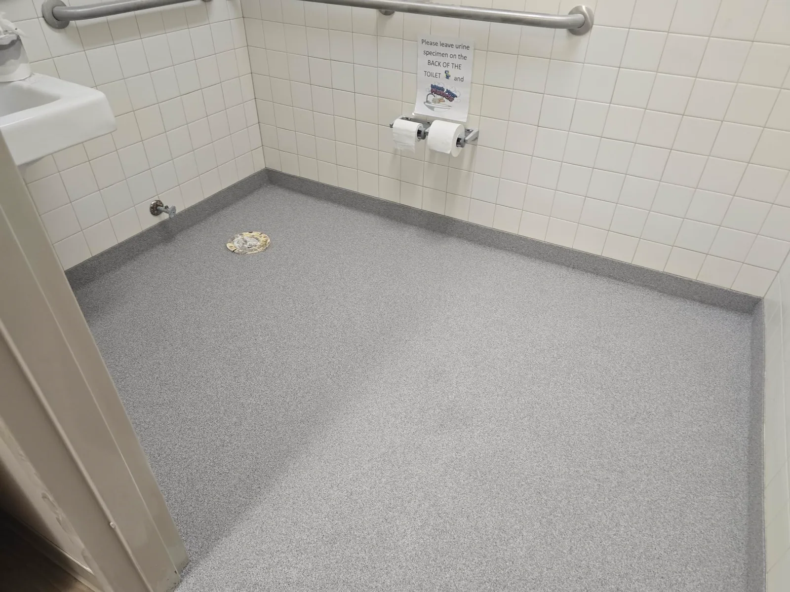 A tiled commercial restroom with a grey quartz broadcast epoxy floor and a floor drain.