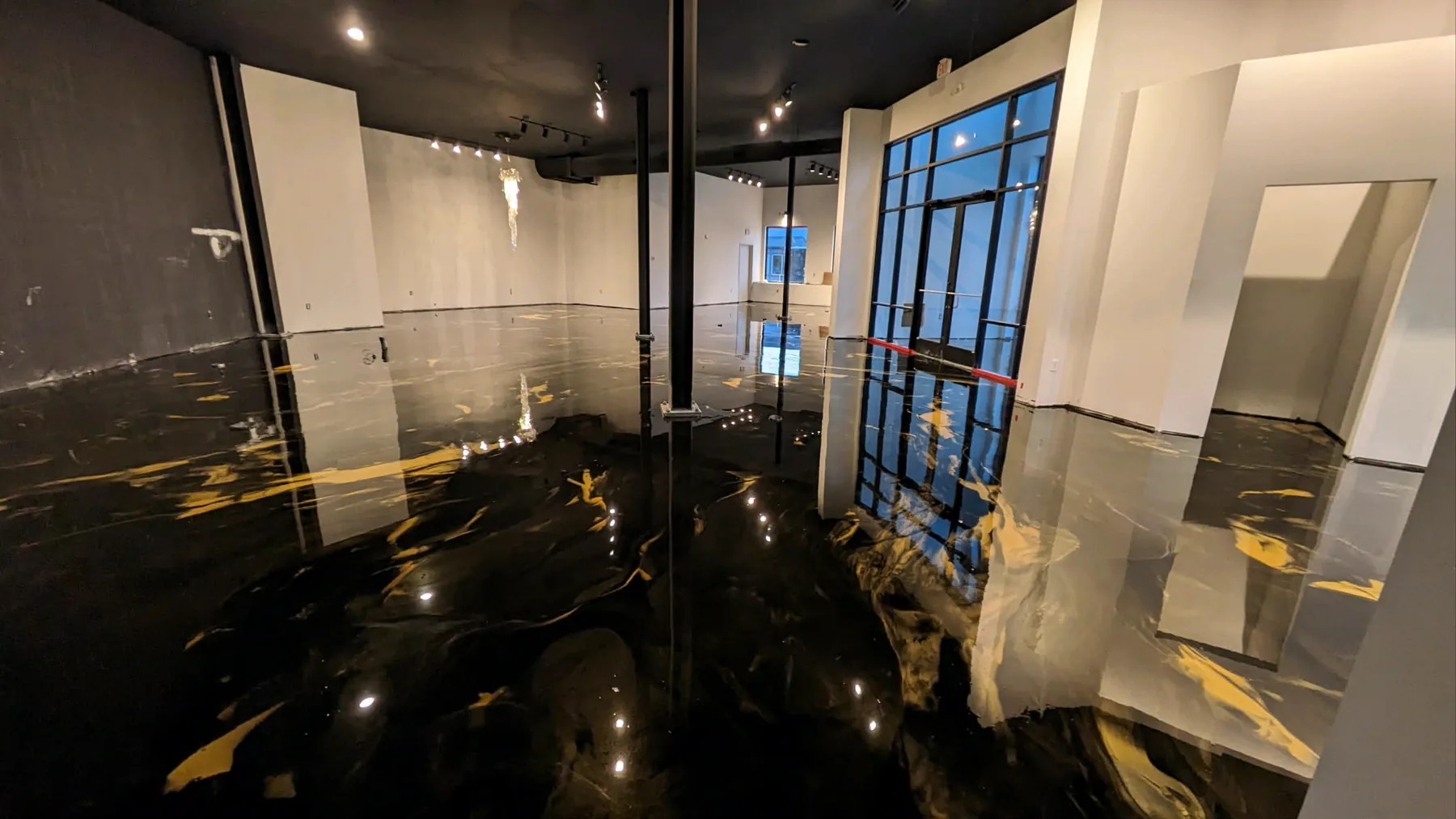 A high-end dress showroom with a black metallic epoxy floor streaked with gold, black ceiling and walls, and a tall steel-framed window.