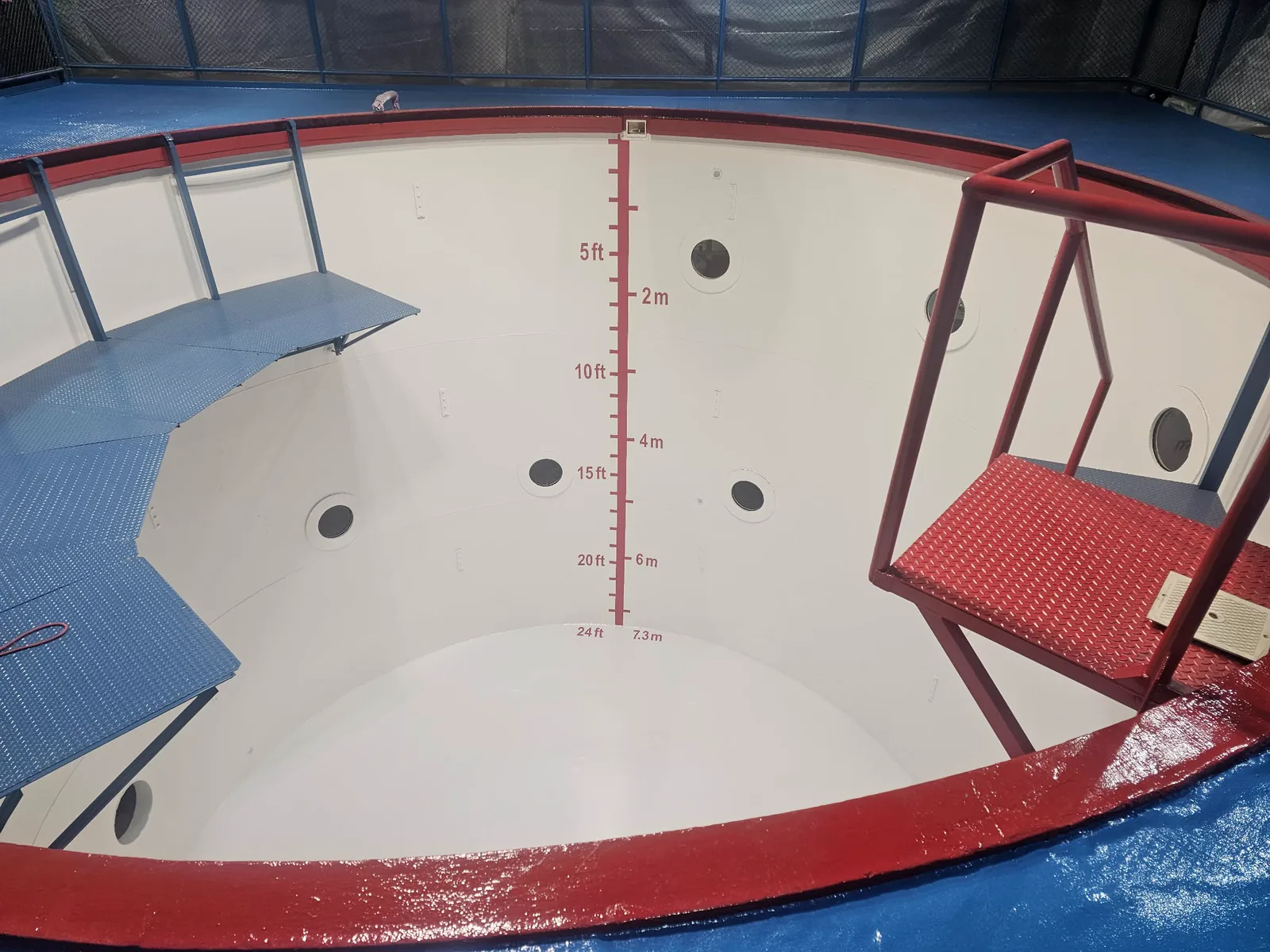 Inside a deep steel dive tank in Huntsville, Alabama, coated white, with red depth markings and blue and red platforms above.